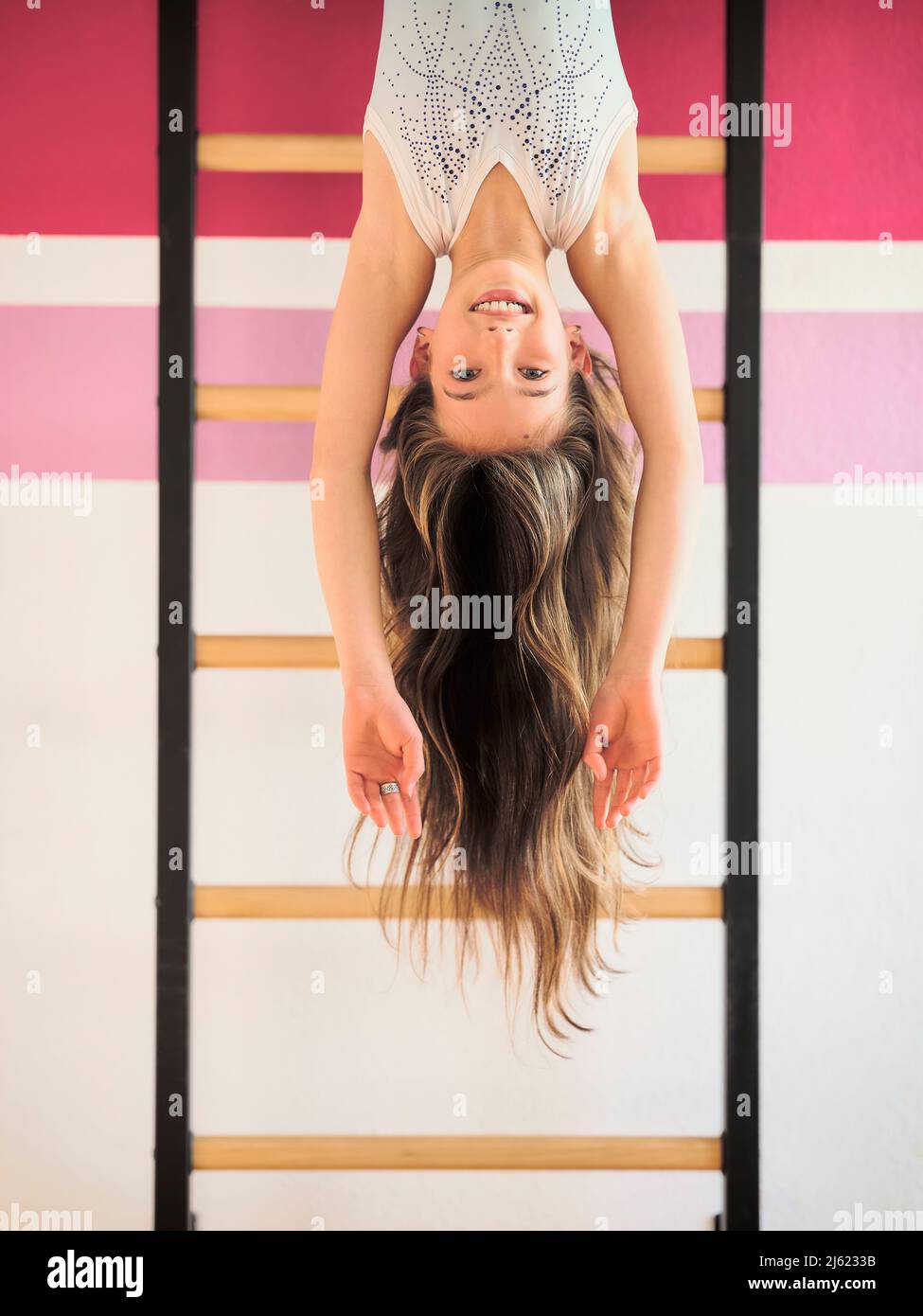 Smiling girl hanging upside down on wall bars Stock Photo
