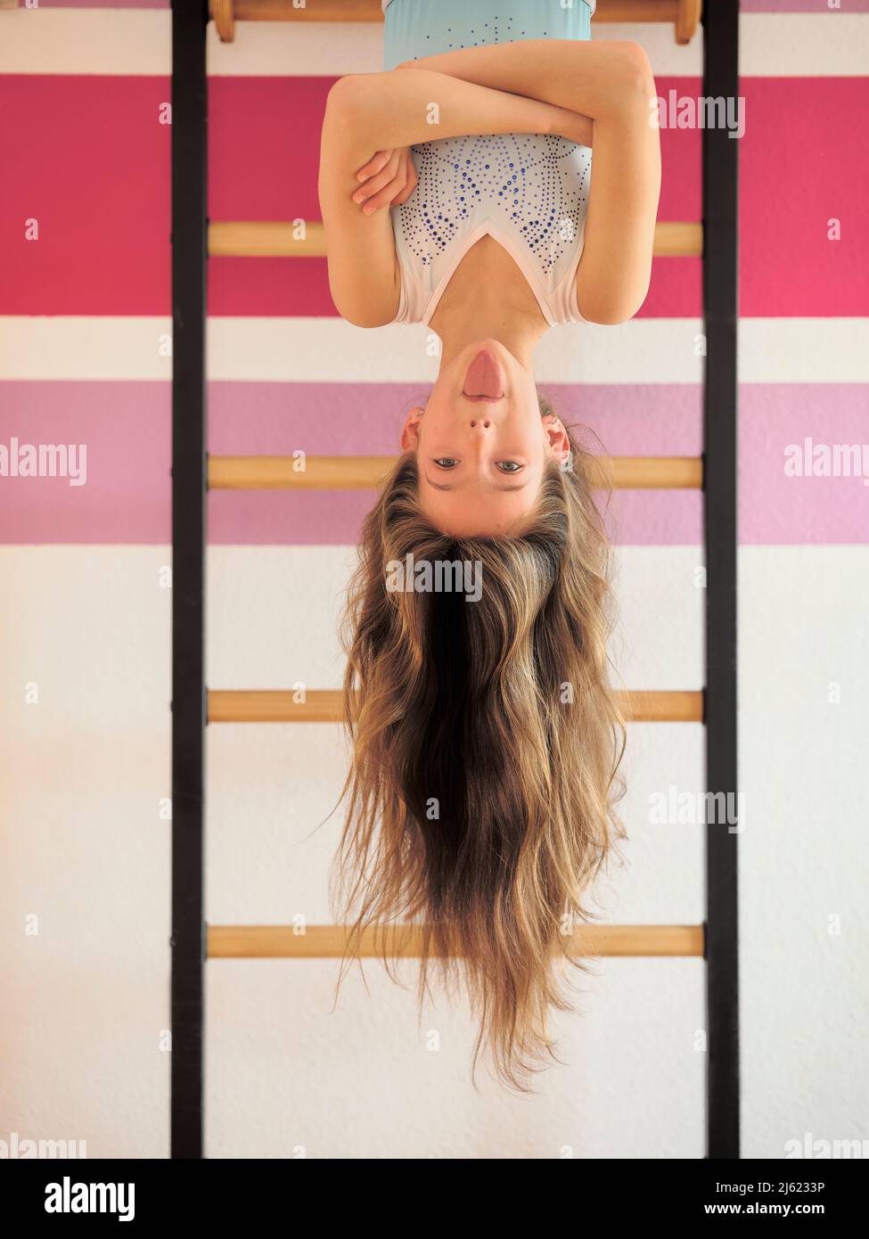 Girl sticking out tongue hanging upside down on wall bars Stock Photo
