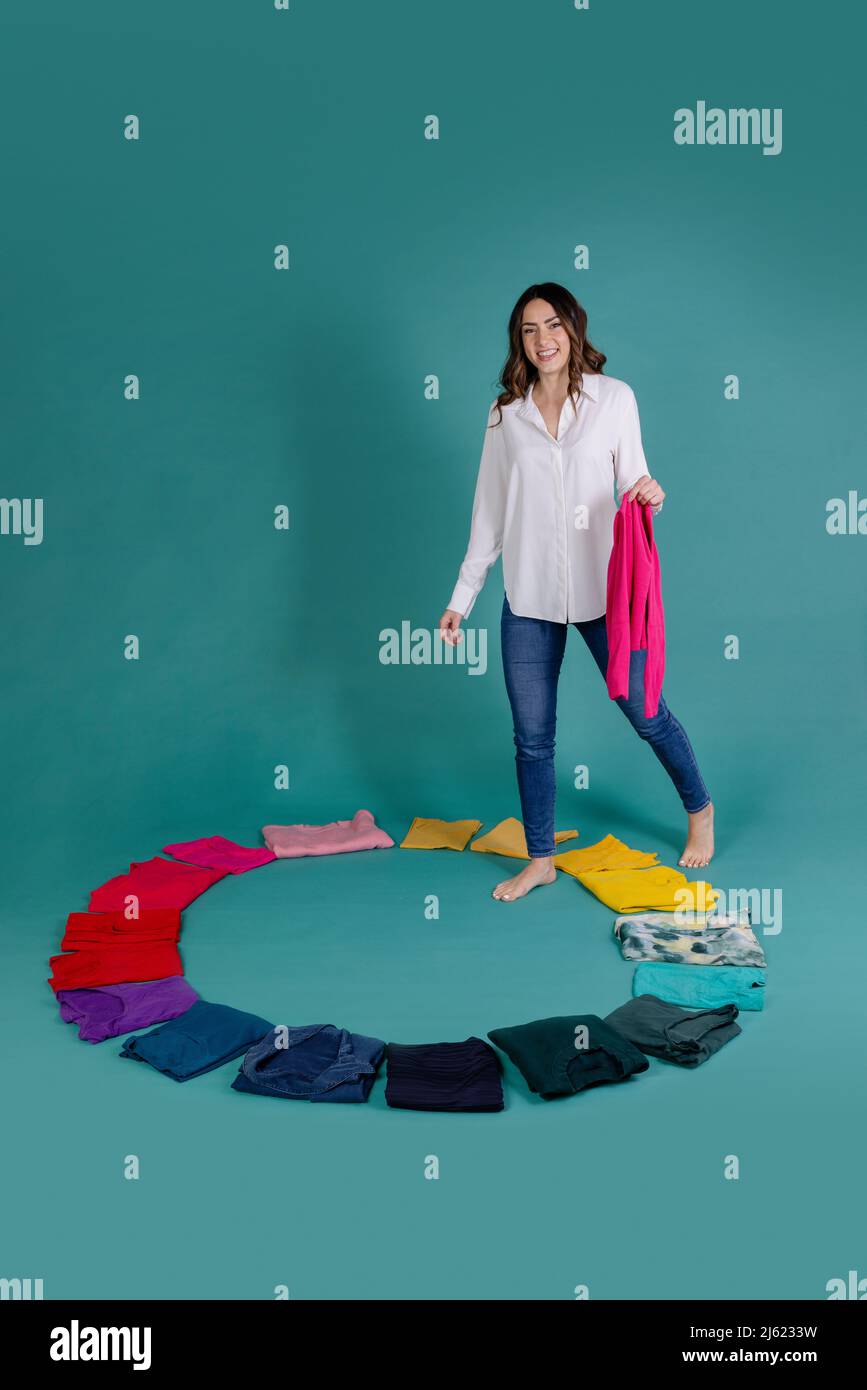 smiling-woman-holding-pink-t-shirt-stepping-inside-circle-made-of-clothes-against-blue-background-2J6233W.jpg