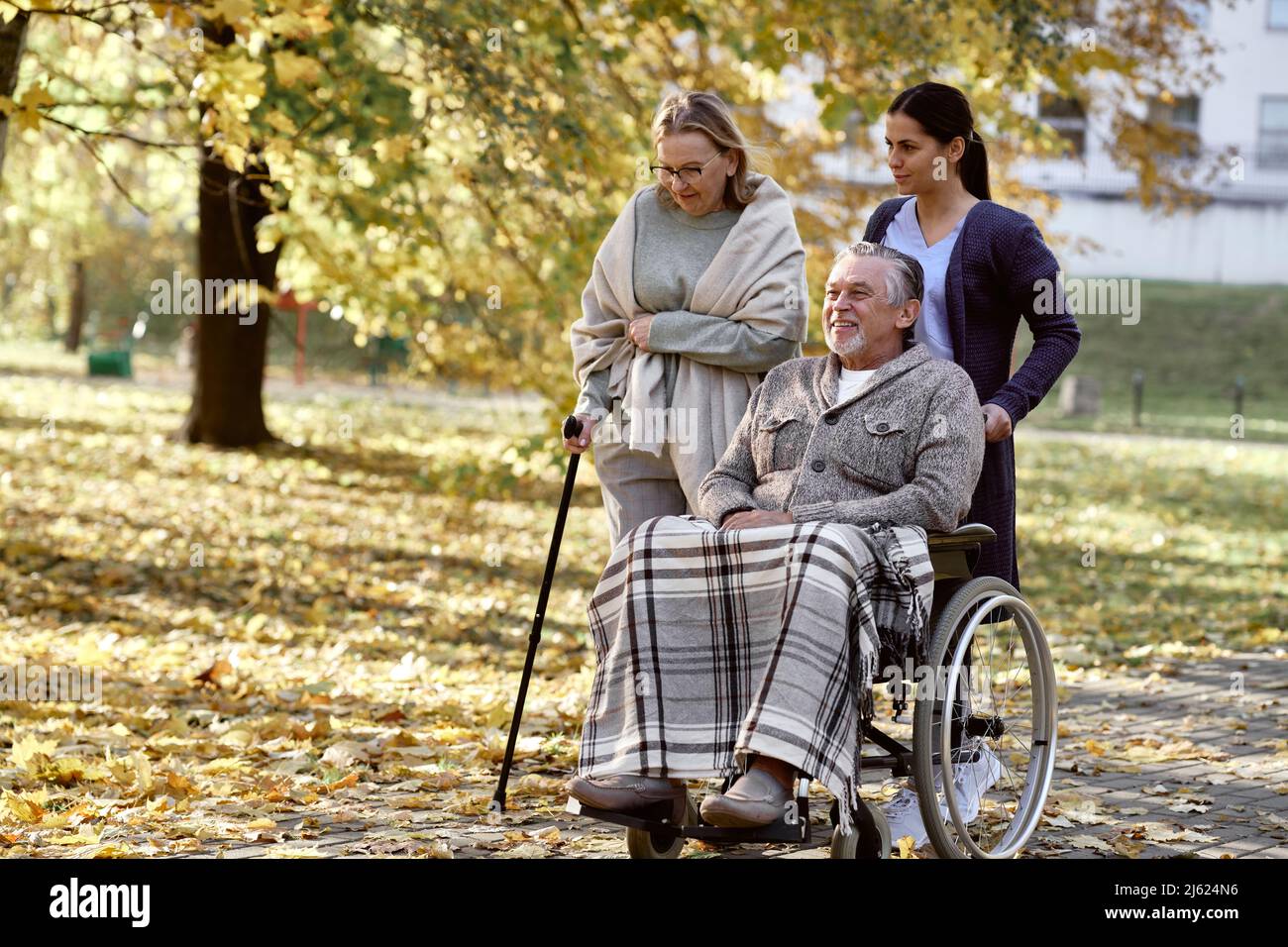 Healthcare worker pushing wheelchair of disabled man by senior woman walking with stick at park Stock Photo