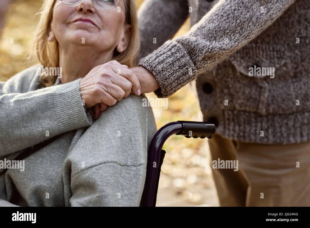 Disabled senior woman sitting in wheelchair consoling man at park Stock Photo