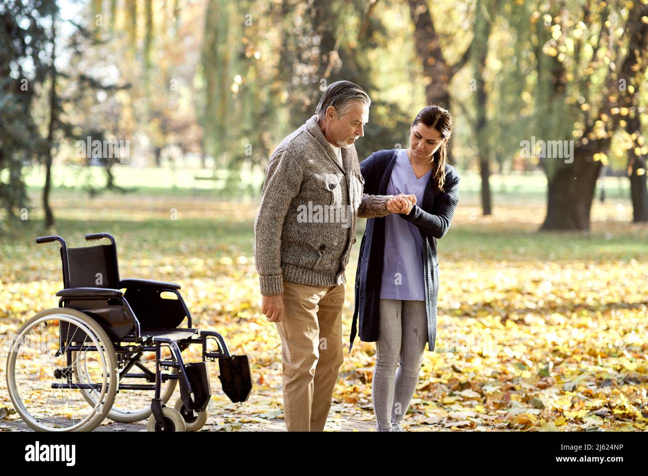 Healthcare worker helping senior disabled man walking at park Stock Photo