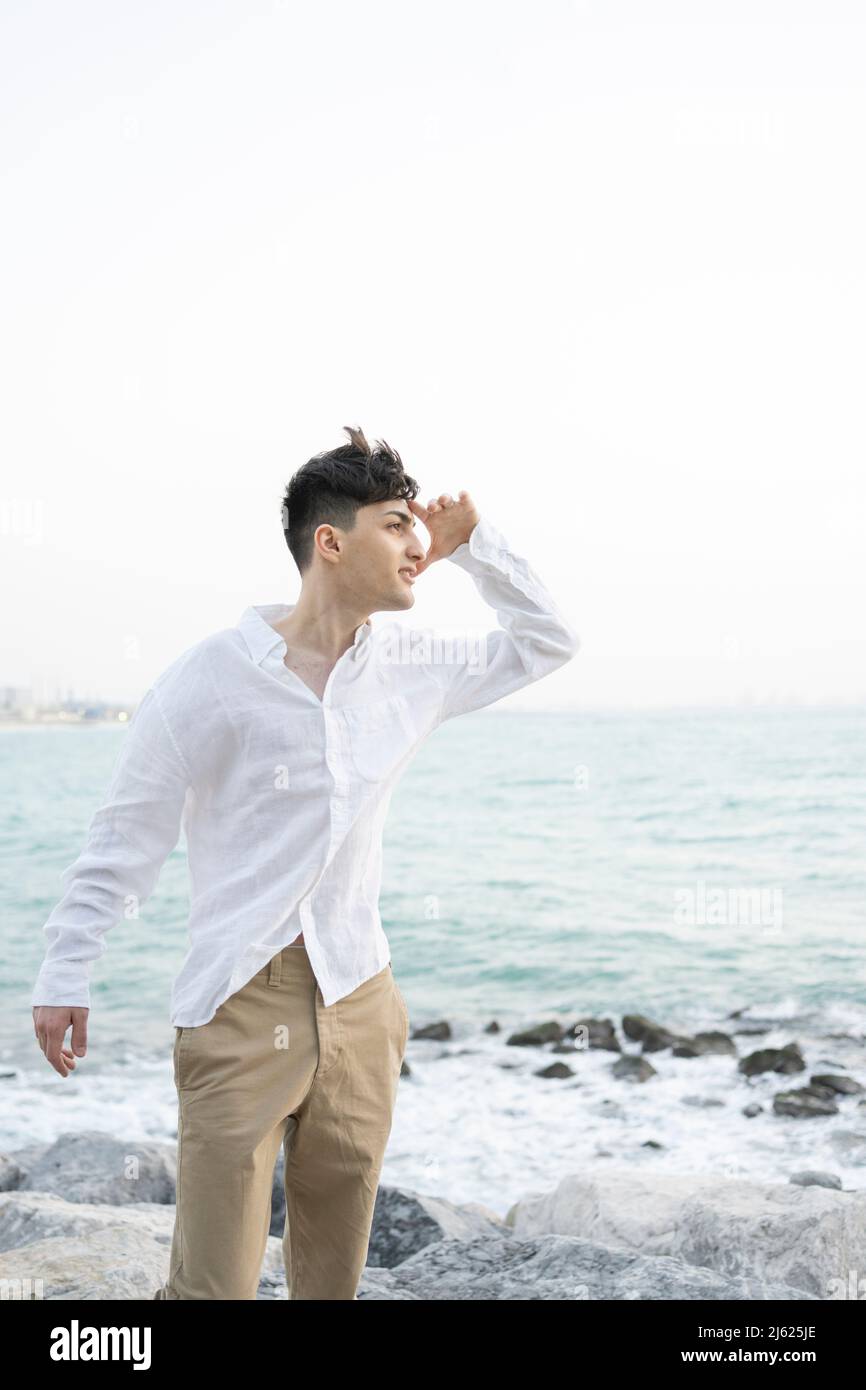 Young man looking at distance standing on rocky beach Stock Photo