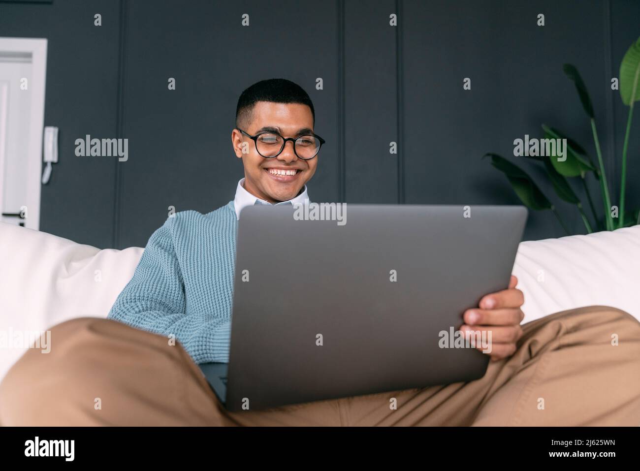 Happy freelancer using laptop sitting on sofa at home Stock Photo