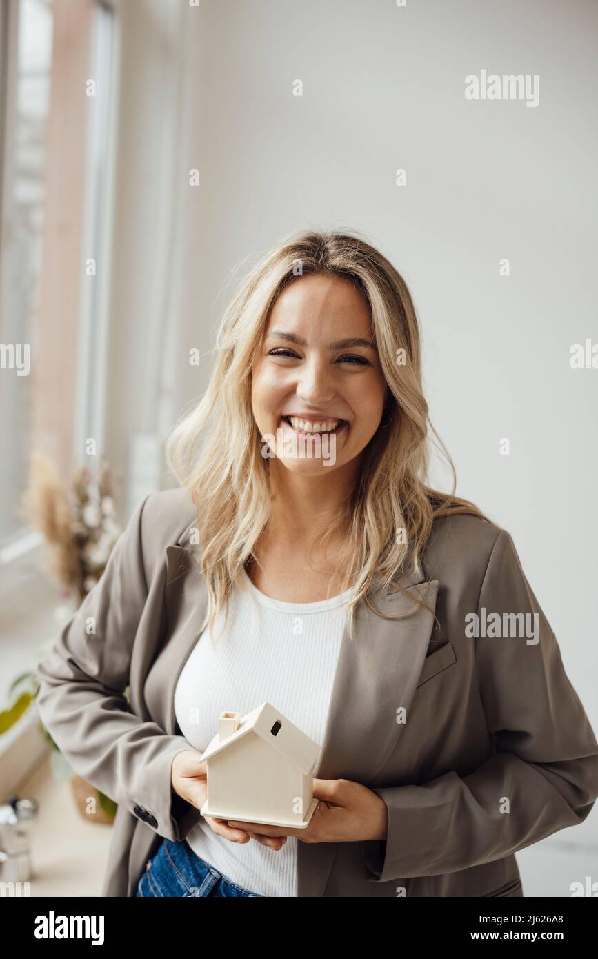Happy businesswoman holding house model standing in office Stock Photo ...