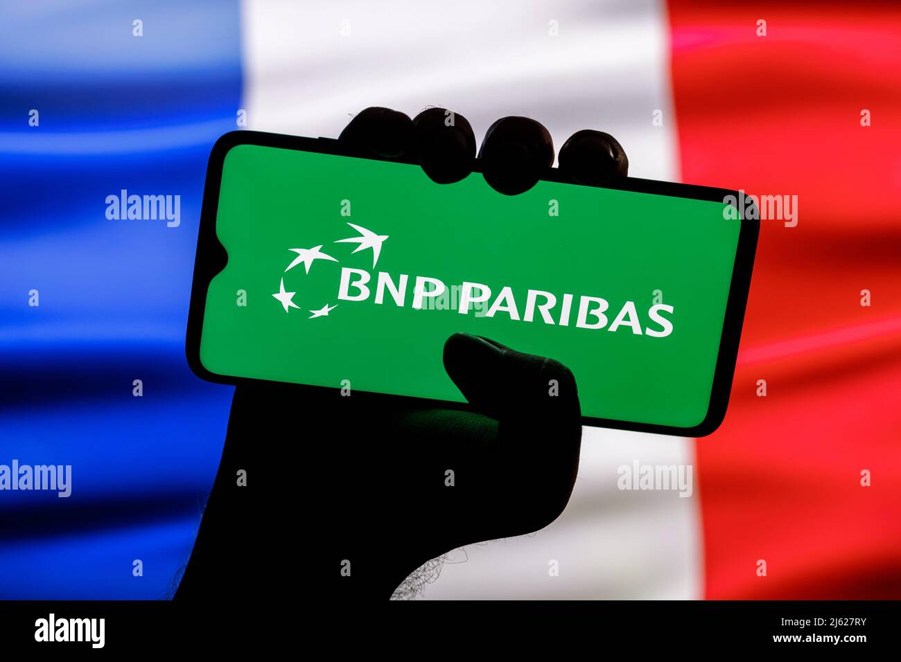 Smartphone with BNP Paribas bank logo in clenched hand on background of France flag Stock Photo