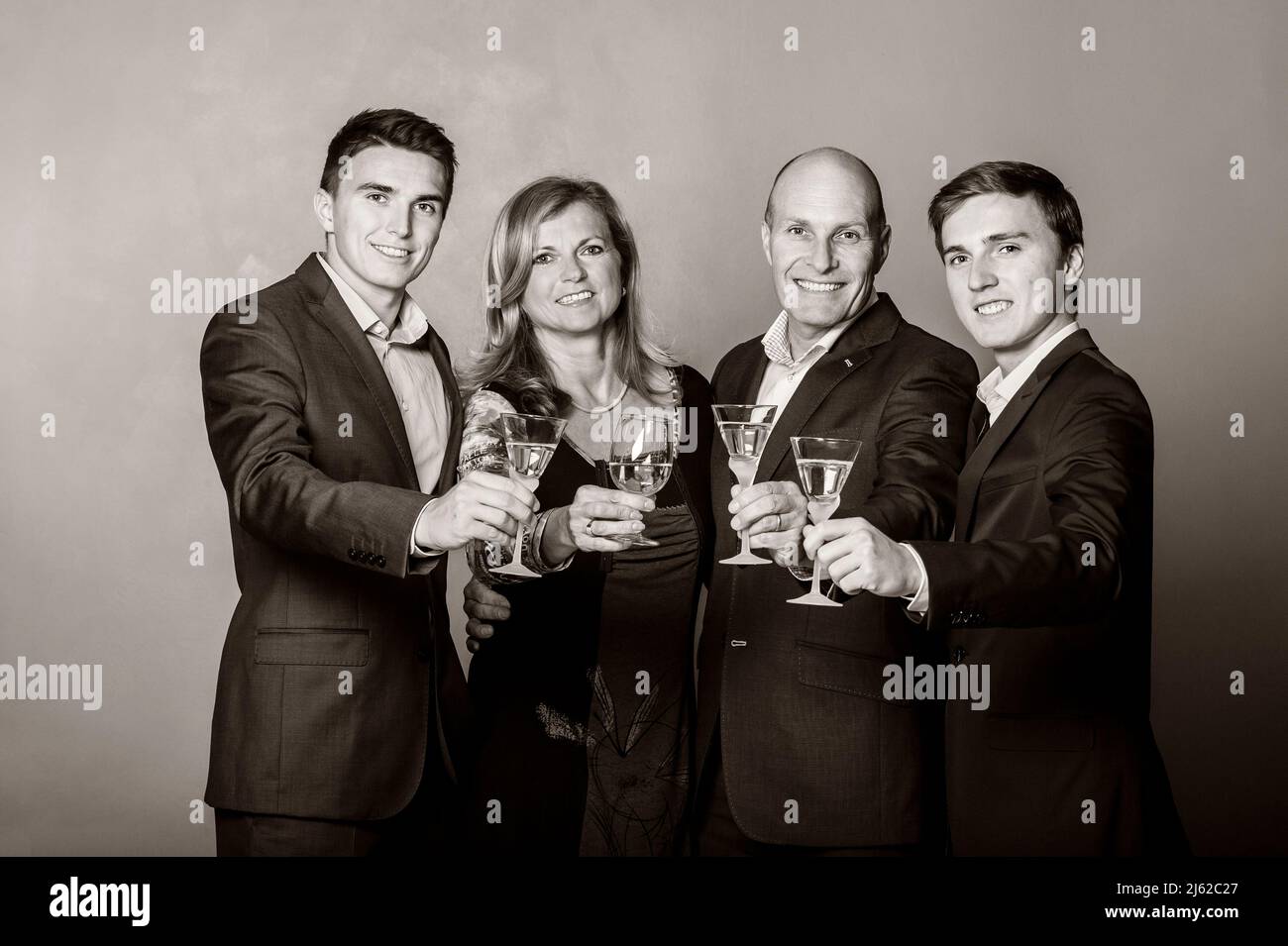 family of four posing in studio in evening dress with glasses of champagne Stock Photo