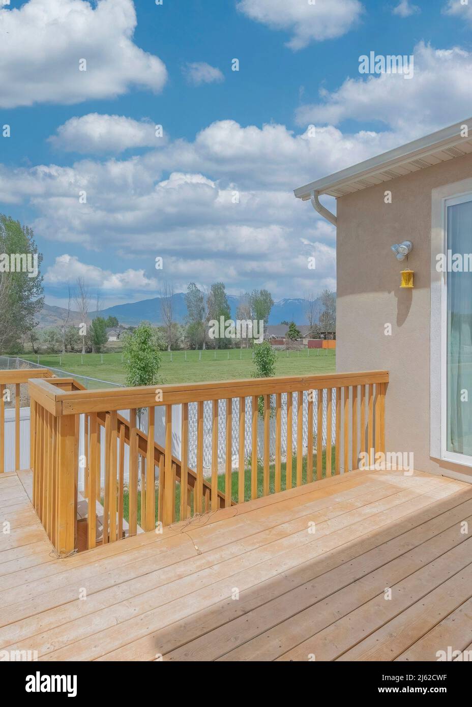 Vertical White puffy clouds Wooden deck of a fenced house with sliding glass door Stock Photo