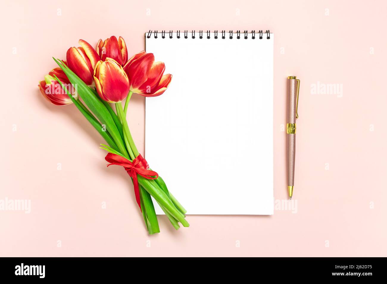 Bouquet of red tulips, notepad on pink background Top view Flat lay Holiday greeting card Happy moter's day, 8 March, Valentine's day, Easter concept Copy space Mock up. Stock Photo