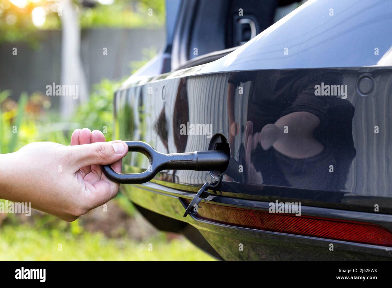 A man twists a towing eyelet into a passenger car to pull the car out