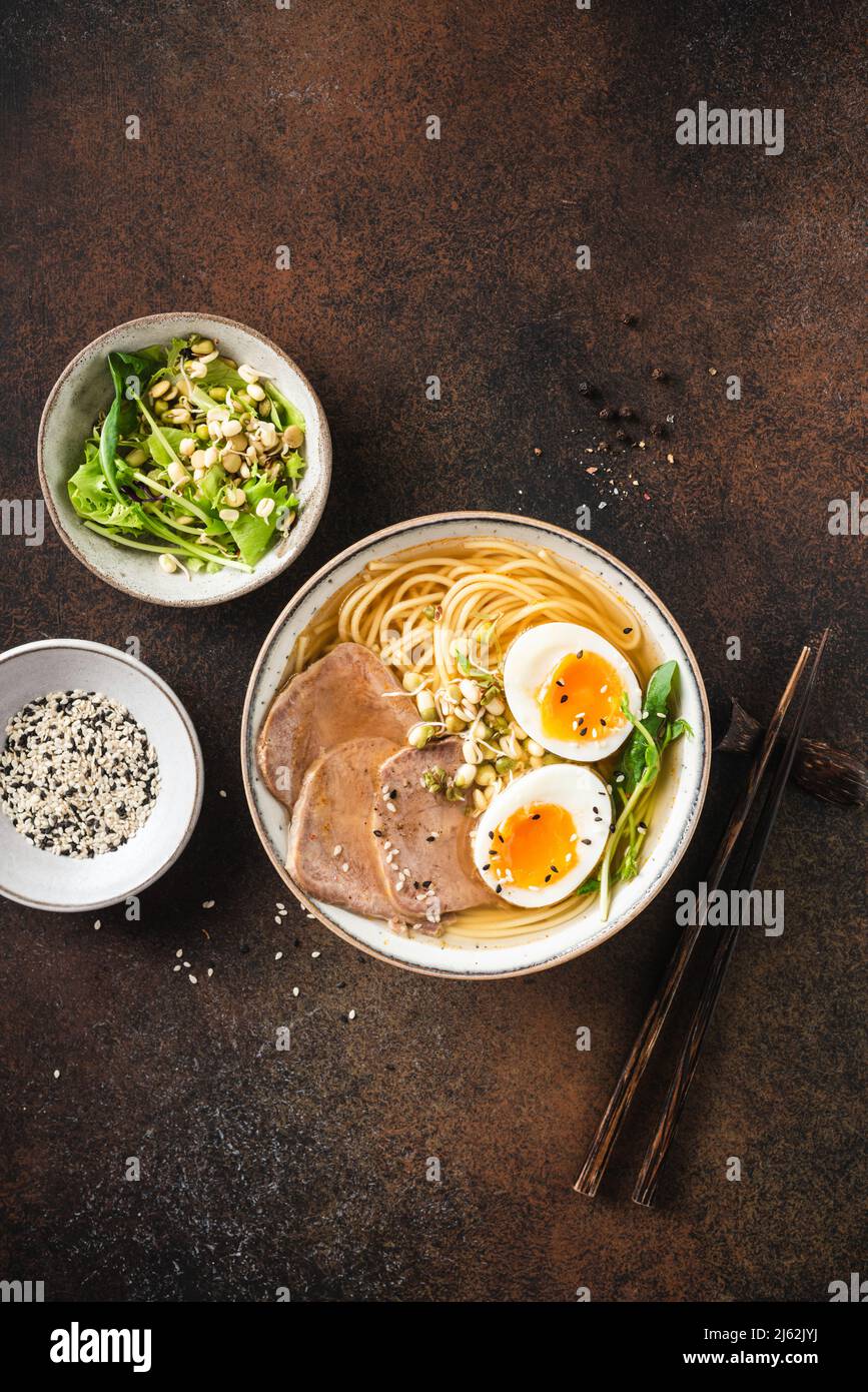 Ramen soup noodle bowl with egg and meat on dark brown background, table top view. Asian cuisine food Stock Photo