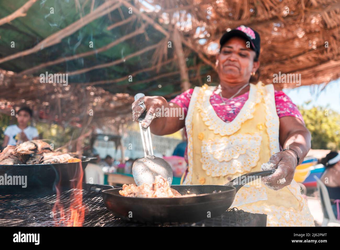 Veretical photo of an elderly Latin woman cooking fried fish on the beach in Masachapa, Nicaragua. Concept of trades, work and activity of older Stock Photo