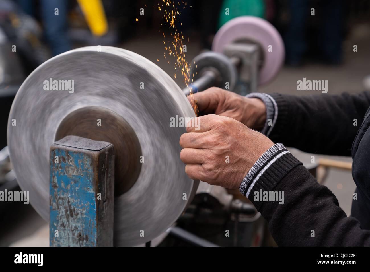 Master sharpens ax on electric sharpener with bright sparks and holds blade with his brutish fingers Stock Photo