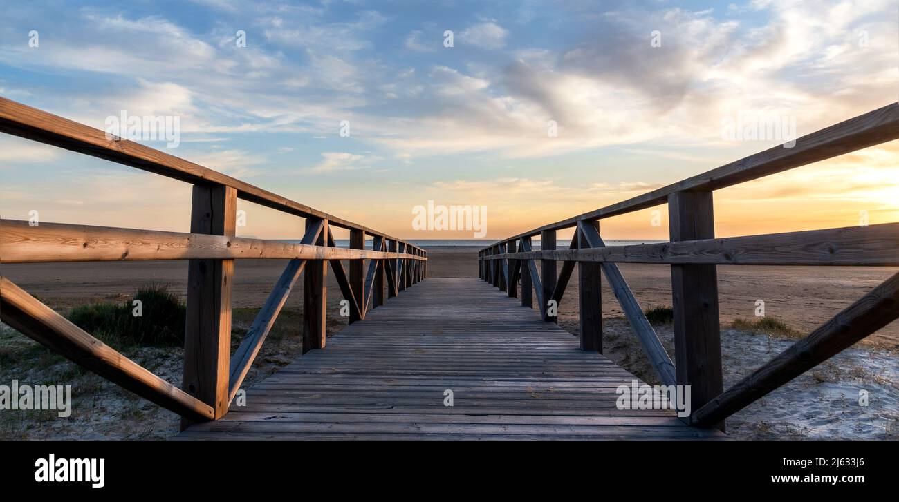 Panoramic view of a wooden walkway leading to the beach at sunset with a beautiful cloudy sky Stock Photo