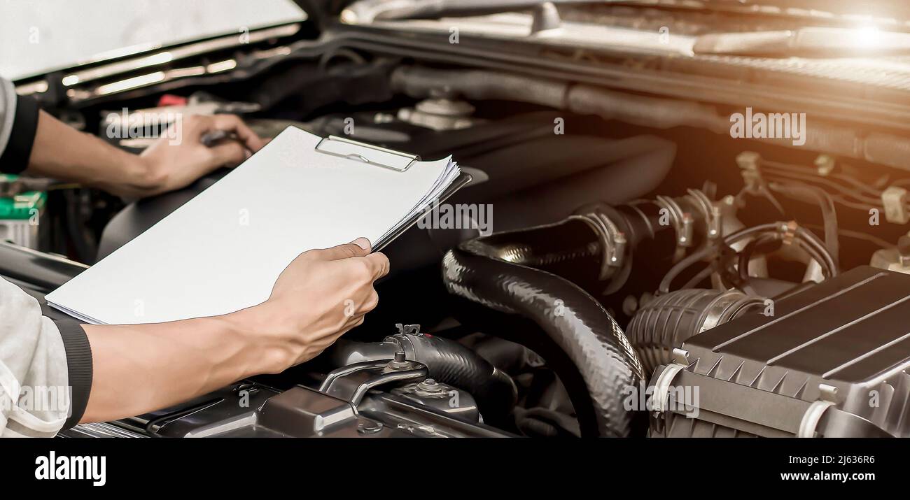 Automobile mechanic repairman checking a car engine with inspecting writing to the clipboard the checklist for repair machine. Stock Photo