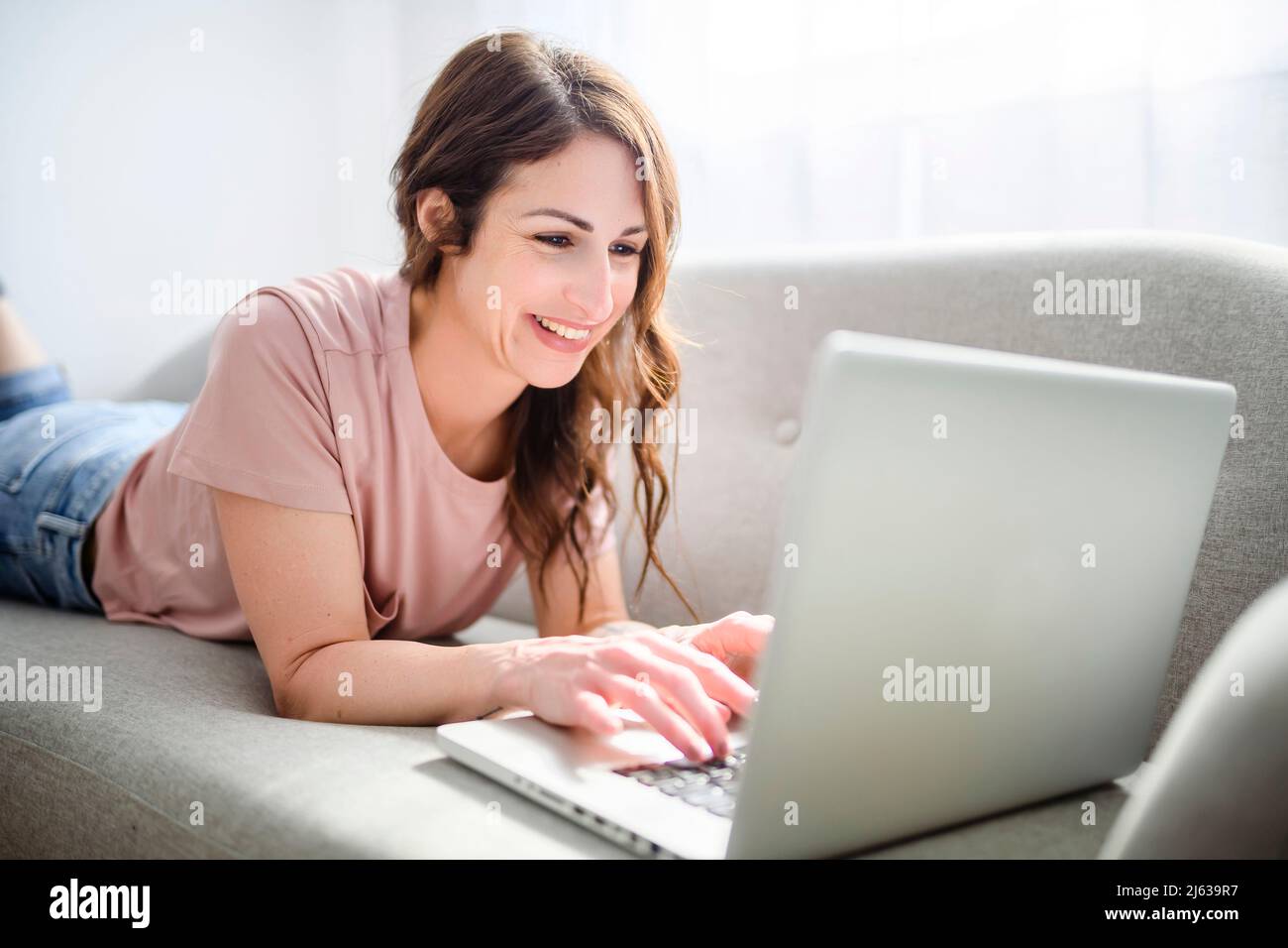 Woman relaxing at home on couch, enjoying free time with laptop on sofa Stock Photo