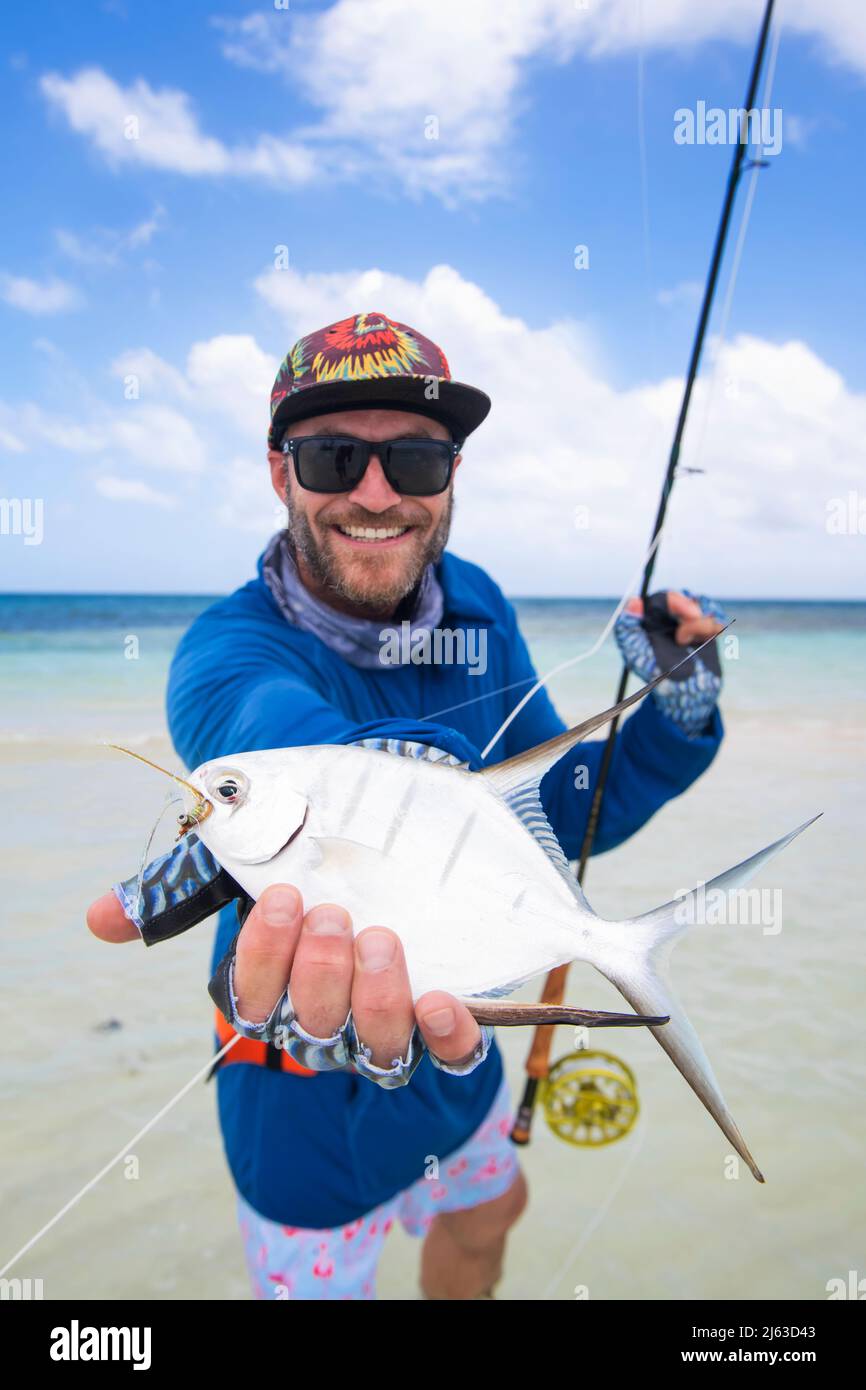 Smiling fisherman swiping his catch on a Caribbean beach. Stock Photo