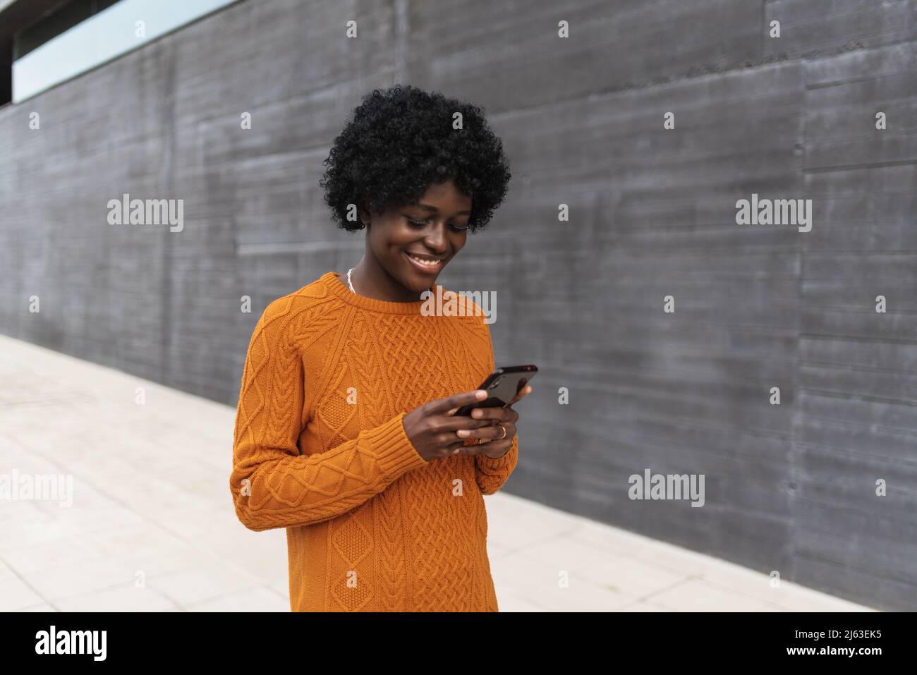 African woman smiling while using her smartphone in the street. Stock Photo