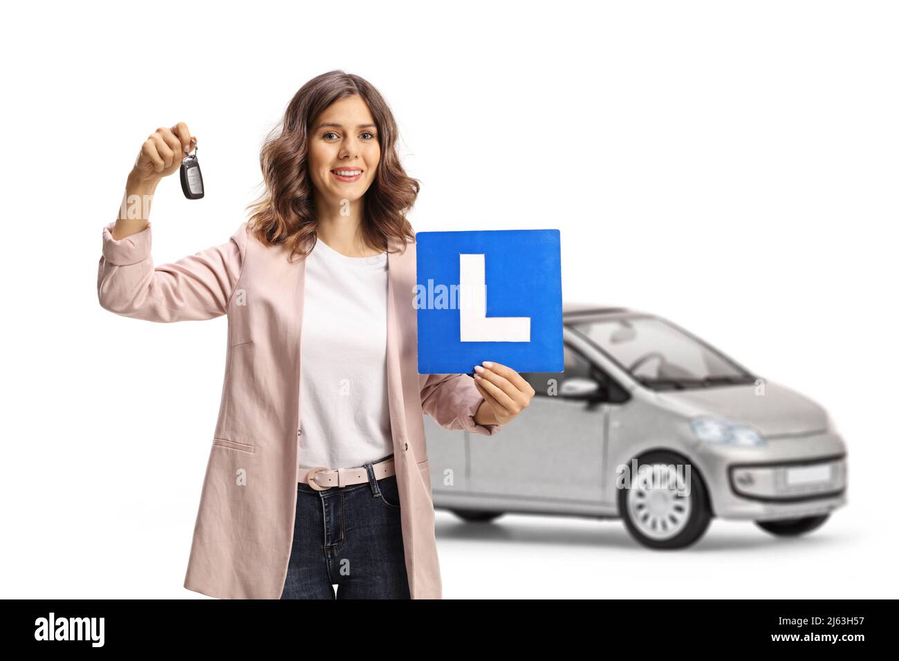 Young woman holding car keys and a learner plate in front of a silver car isolated on white background Stock Photo