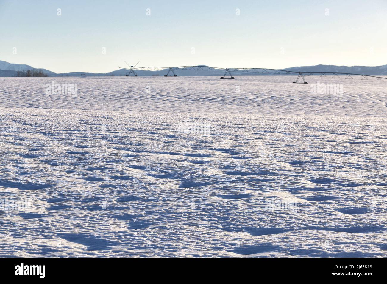 Snow patterns caused by the wind blowing across a farm field, with farming equipment out of focus in the background.  The snow will provide water for Stock Photo