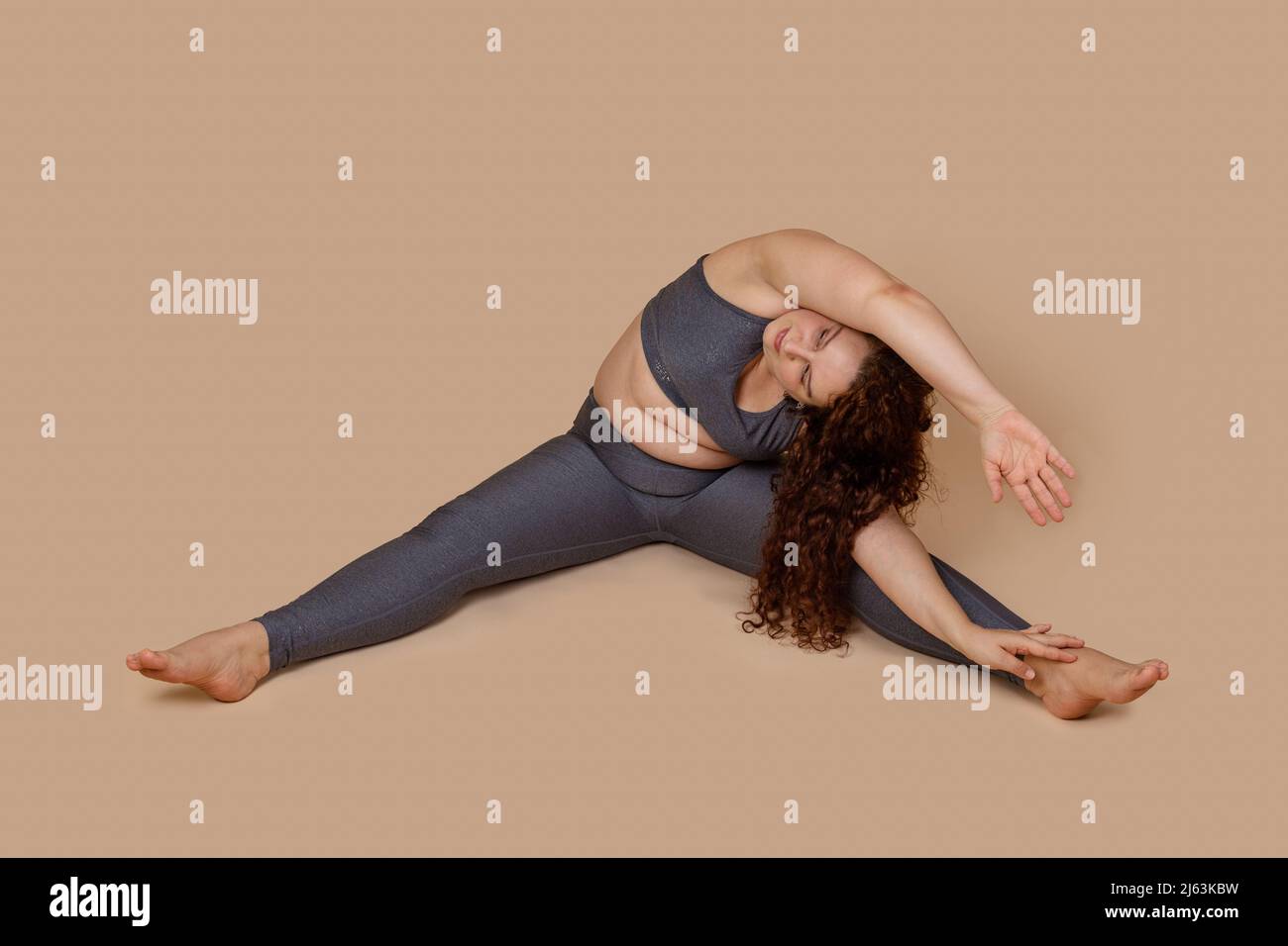 Concentrate curly haired, barefoot woman corpulency doing sports gymnastics incline with arms to right. Self acceptance Stock Photo