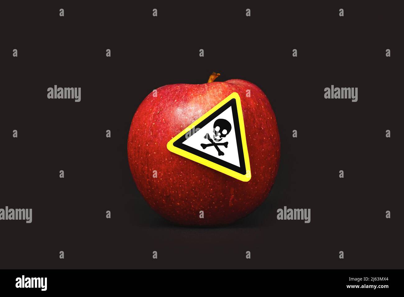 Concept for pesticide residues in agricultural food products dangerous to humans. A red apple with poison symbol sticker on black background Stock Photo