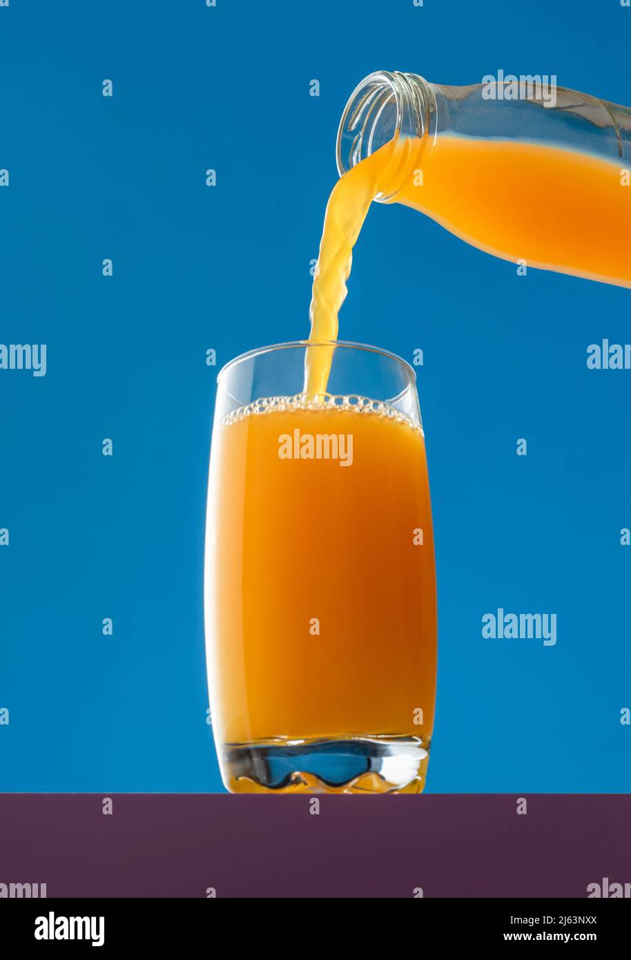 https://c8.alamy.com/comp/2J63NXX/pouring-orange-juice-from-a-bottle-into-a-glass-isolated-on-a-blue-background-low-angle-view-with-a-glass-of-fresh-orange-juice-2J63NXX.jpg