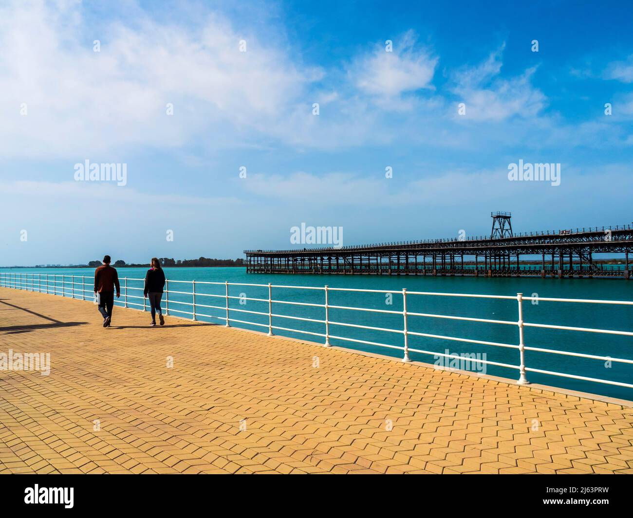 Eterosexual couple walking along the Muelle del Tinto of the Odiel river in Huelva, on a sunny day. Stock Photo