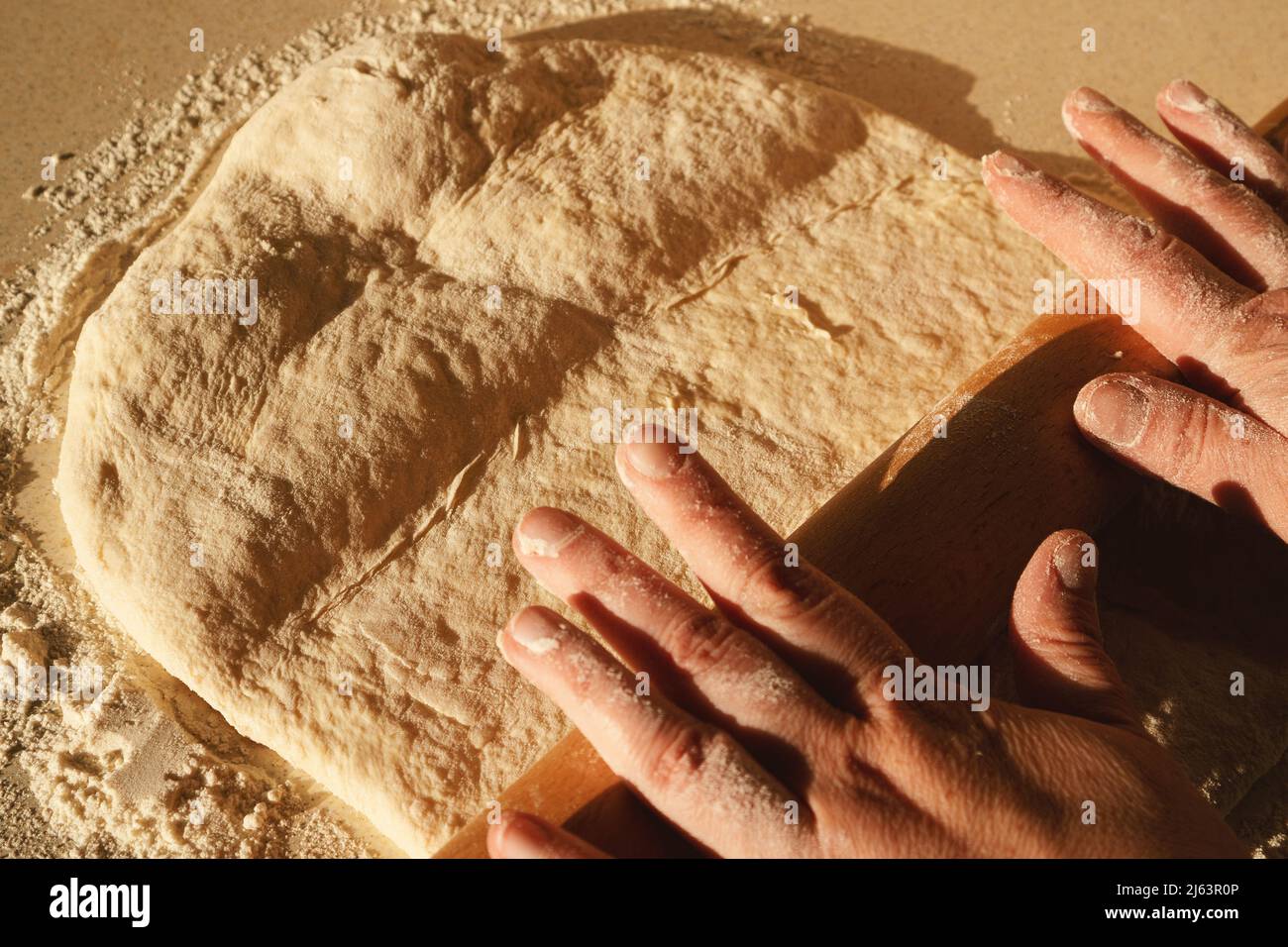 Preparing the dough for bread, kneading the dough with a rolling pin on the table. Stock Photo