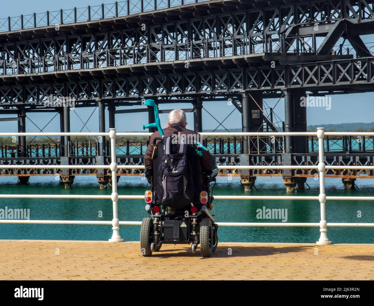 An elderly man in a wheelchair enjoying a walk along the Odiel river in Huelva, on a sunny day. Stock Photo