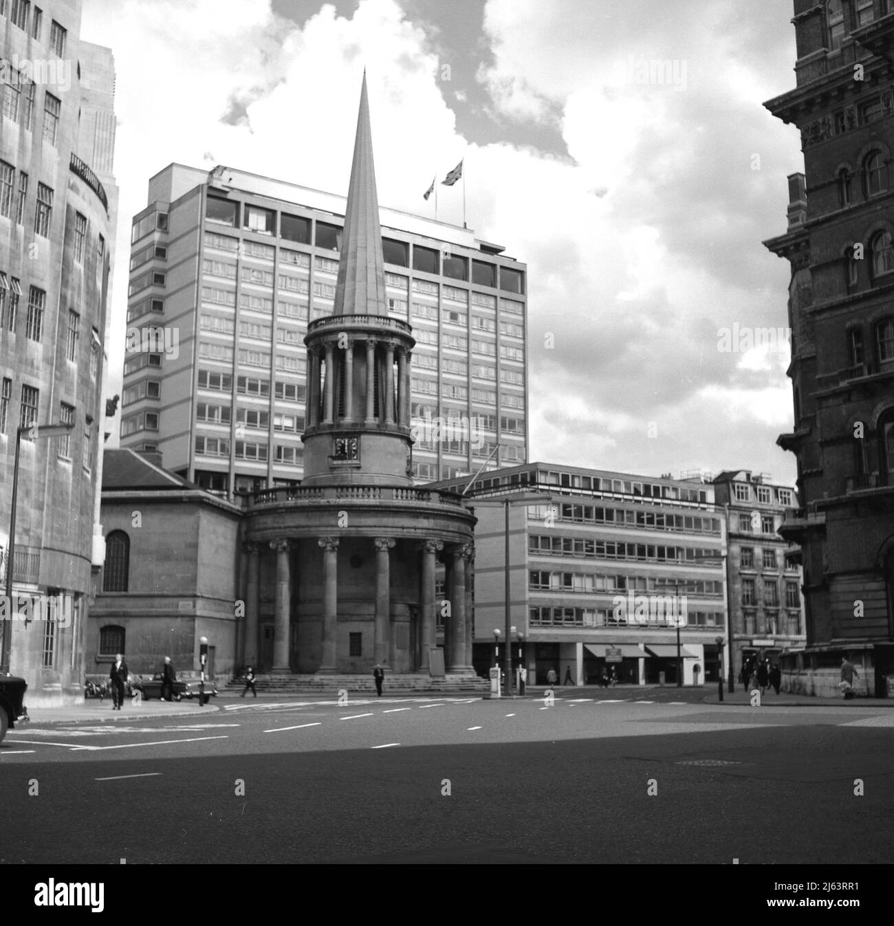 1960s, All Souls church at Langham Place, Marylebone. On the left of the picture, Broadcasting House, headquarters of the BBC in London. With its distinctive spired circular vestibule, the church was built in the Regency style in 1824 from a design by John Nash. Behind the church, modern office blocks of the era, certainly not in any recognised architectural style, but a standard rectangular shape and built of pre-cast concrete panels with extensive windows. So callled 'modernism' in style, this dull building design was repeated all over London in the 1960s, being cheap and quick to build. Stock Photo