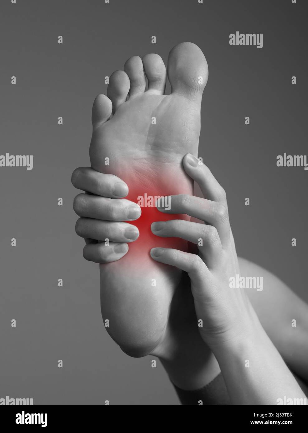 Arch pain caused by inflammation, overuse, plantar fascia injury. Woman hands holding foot with red point. Black and white. Orthopedic complaints and health problems concept. High quality photo Stock Photo