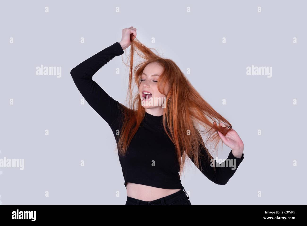 young woman with tousled hair stretches on a light background Stock Photo