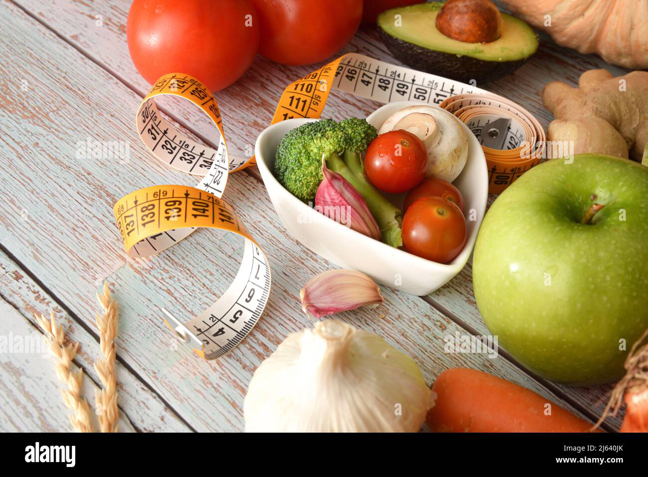 Healthy eating weight control concept with fruits and vegetables in heart shaped bowl and around and measuring tape on wood detail. Elevated view. Hor Stock Photo