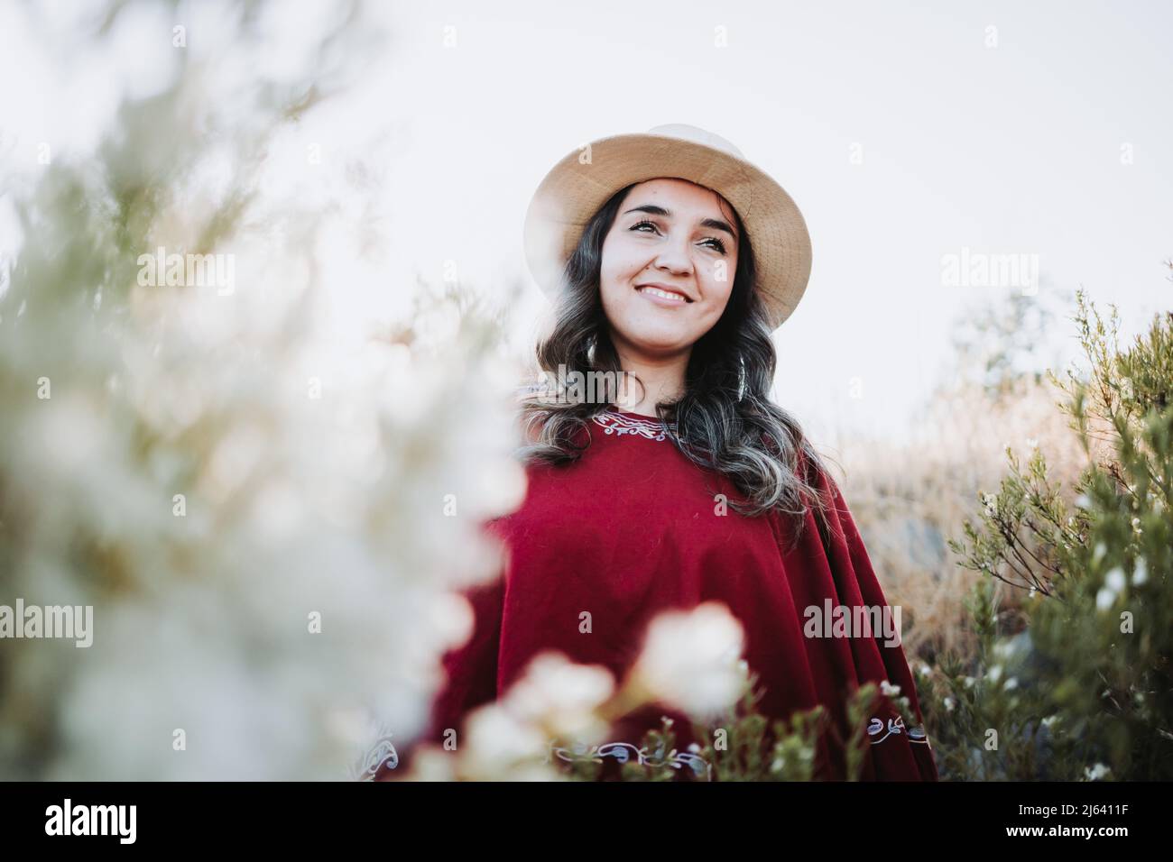 Traditional latin american woman wearing a red poncho and a hat seen from behind, in a natural space. Womens empowerment Stock Photo