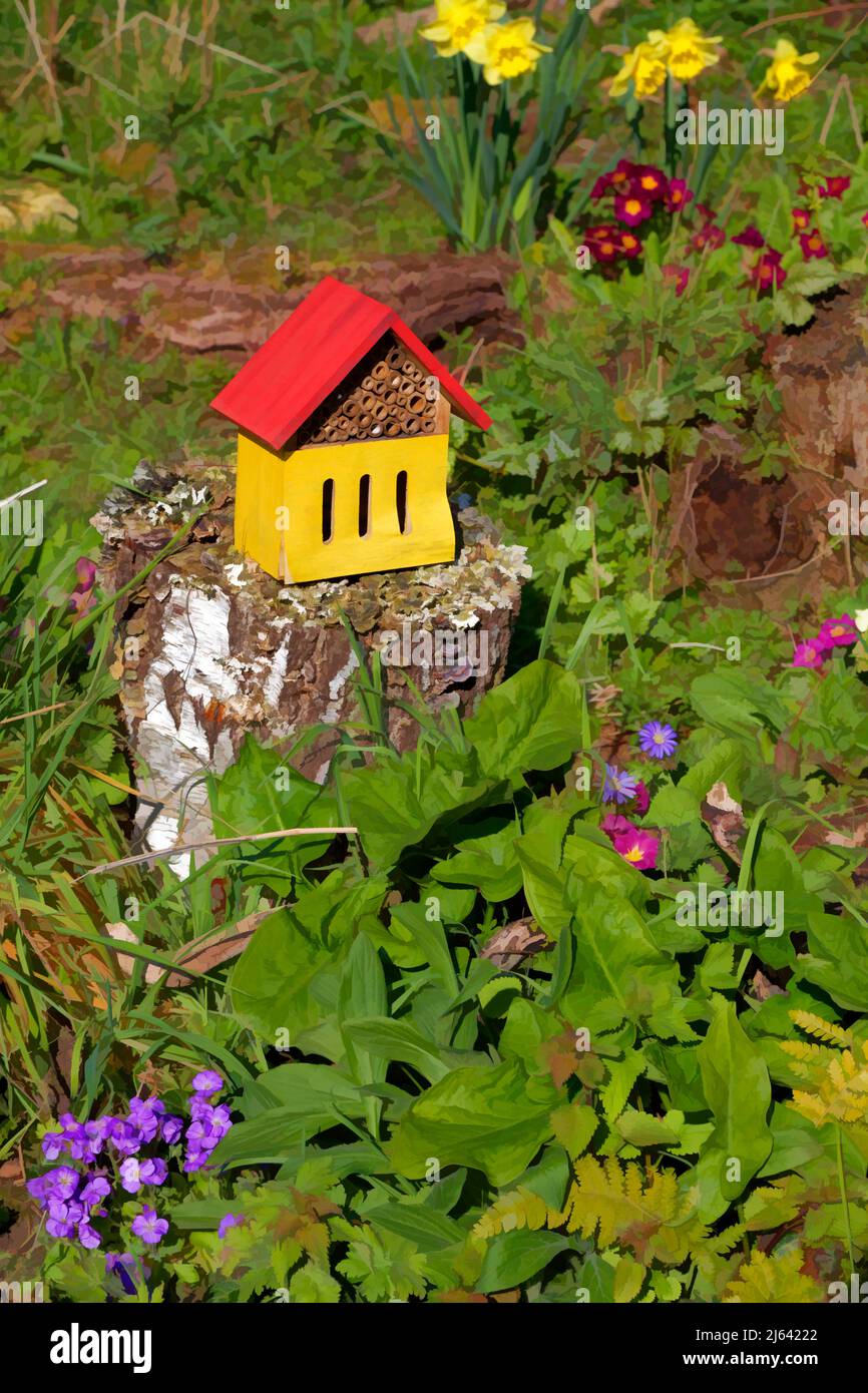 Bug hotel on a tree trunk with flowers in a nature garden. Stock Photo