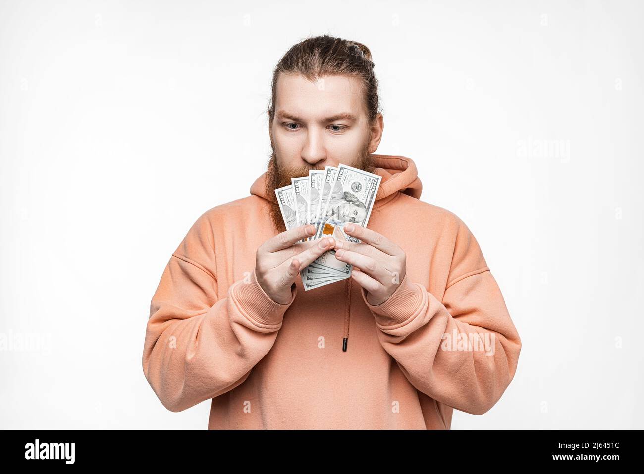 Handsome scandinavian man holding dollar currency money in his hands on gray background. Guy with ginger hairstyle and beard in a sweatshirt. The conc Stock Photo