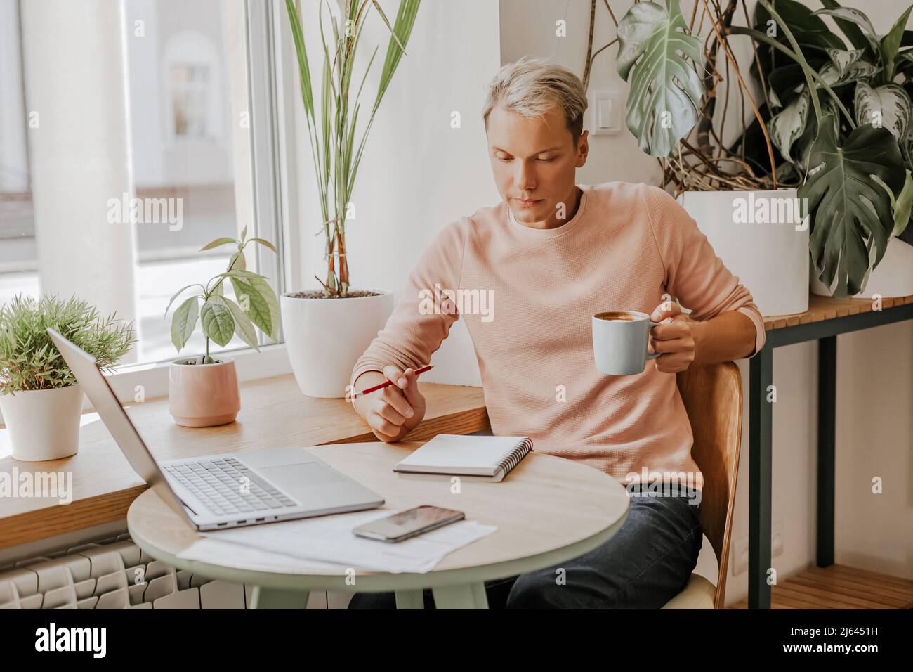 Man works in the workplace with documents and and drinks coffee in an eco cafe with plants Stock Photo