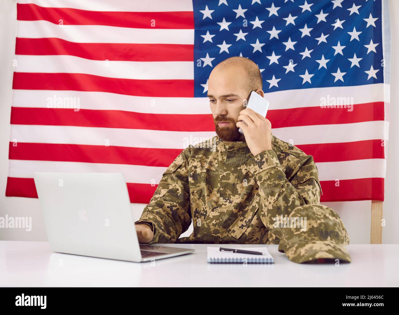 American military man uses laptop, mobile phone and notebook to work in headquarters building. Stock Photo