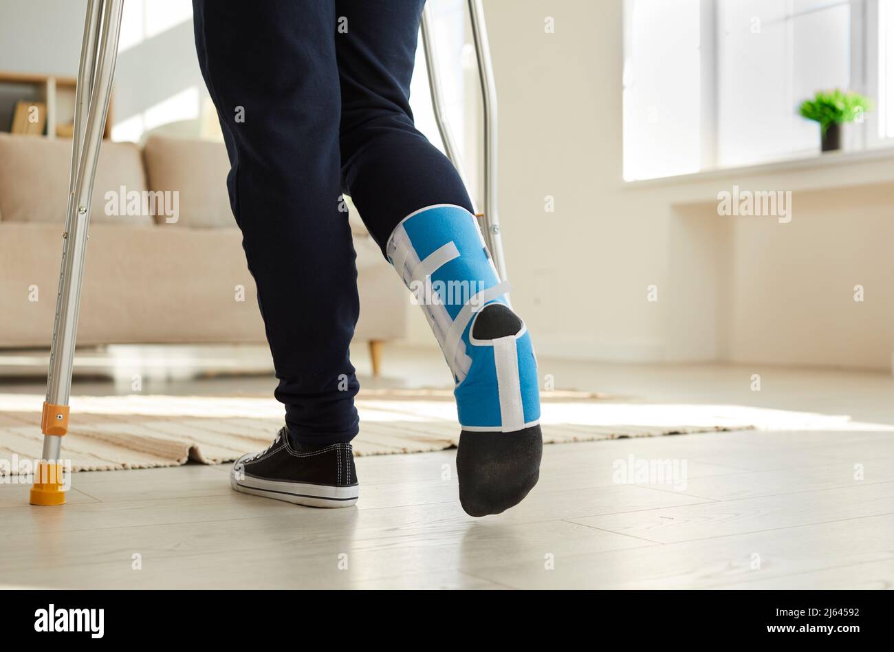 Young man wearing support brace on his injured foot and walking on crutches at home Stock Photo