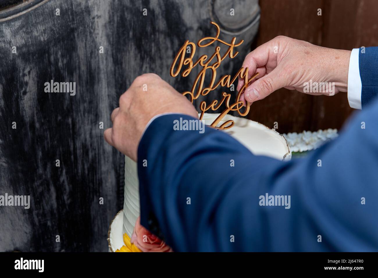Hands of the groom finding the center of the wedding cake to properly place the topper with clever quote. Stock Photo