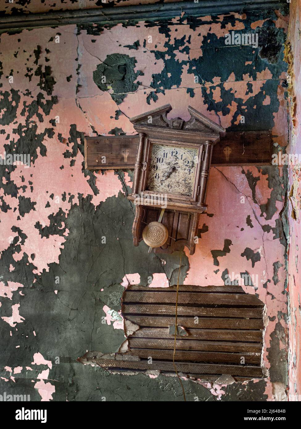 A crooked clock and an old plaster wall showing the layers of paint are fixtures in this abandoned house. Stock Photo