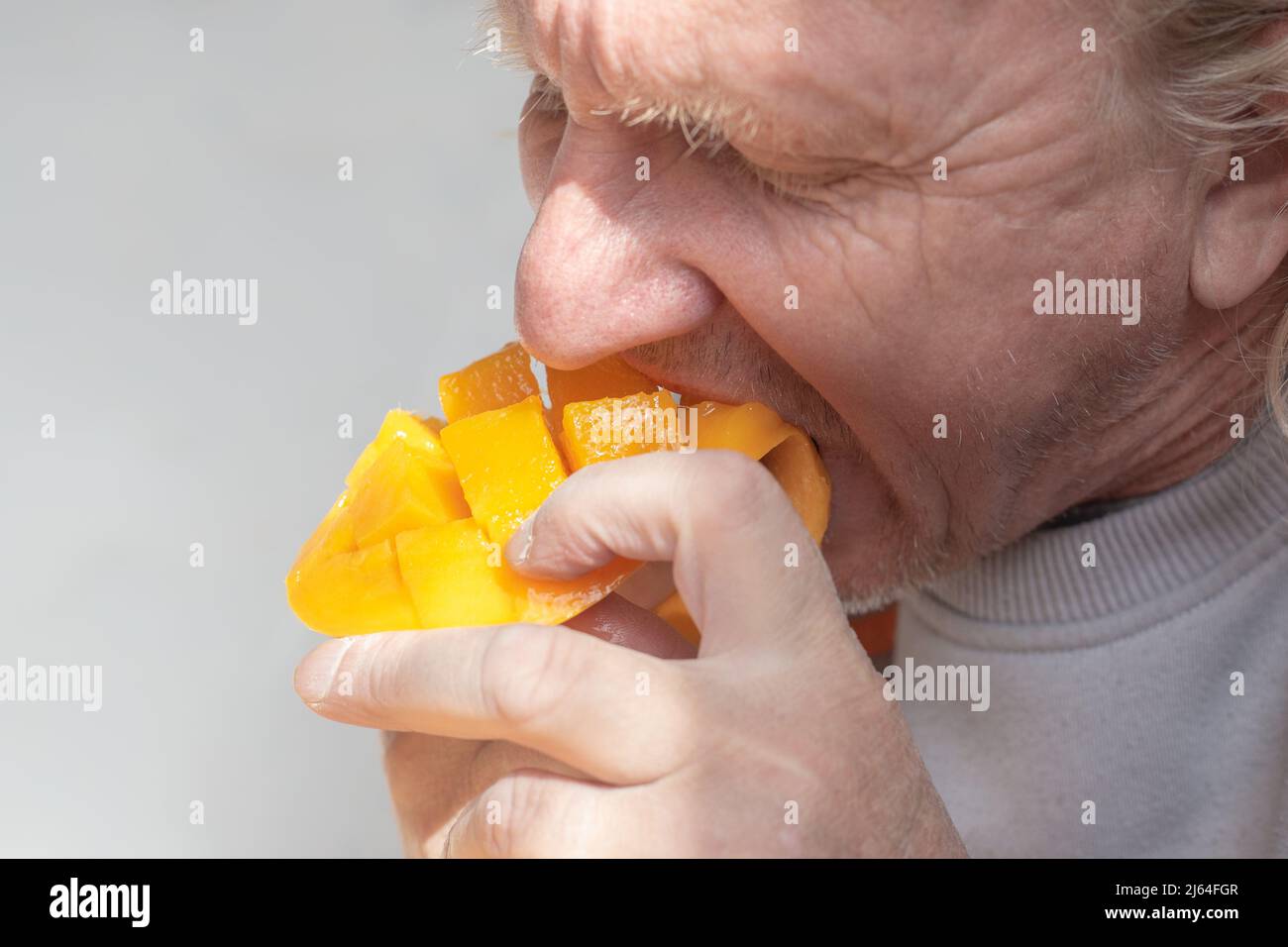 Mature man eats a ripe yellow mango. Close-up of the face. Stock Photo