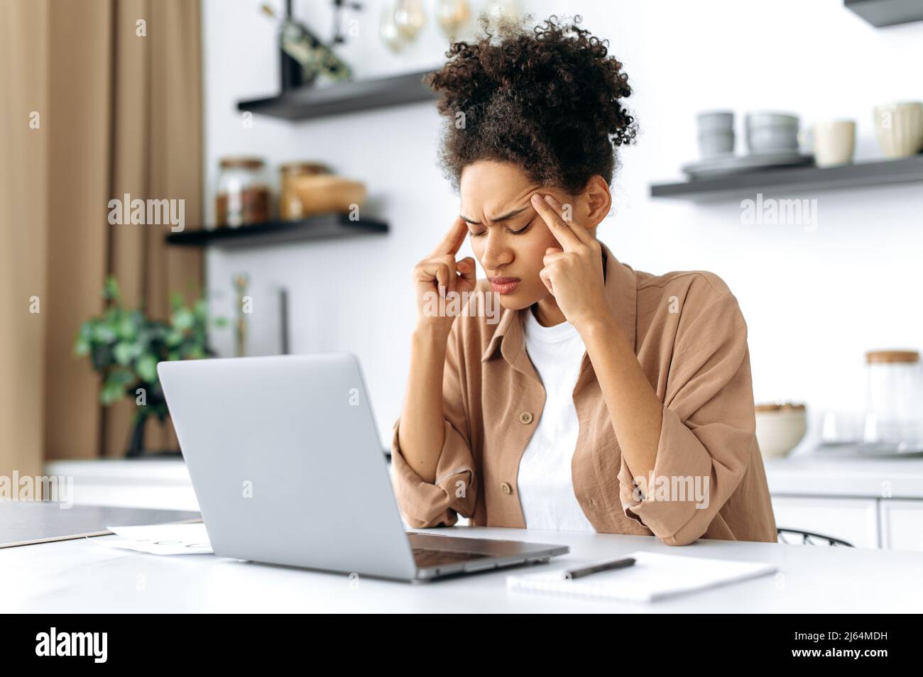 Overworked frustrated sad african american girl, student or freelancer, in casual clothes, studying or working at home uses laptop, experiencing stress, suffering of headache, migraine, need rest Stock Photo