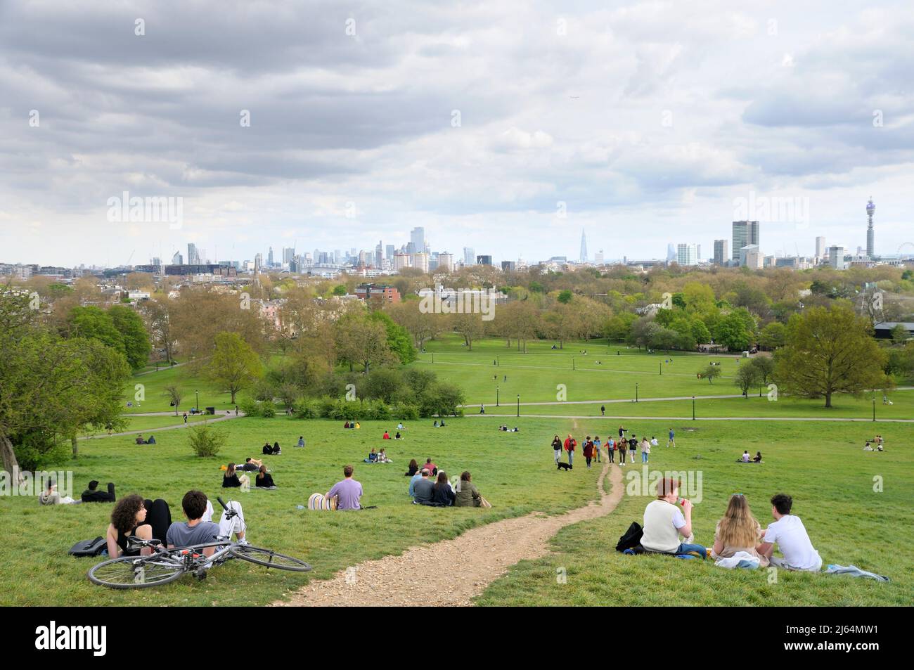 People relaxing on the grassy slopes of Primrose Hill park with uninterrupted views of famous buildings on the London skyline, North London England UK Stock Photo