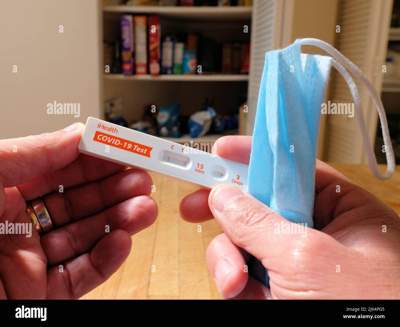 Person's hand holding an iHealth COVID-19 Antigen Rapid Test in-home self test card displaying a negative Coronavirus result; with surgical facemask. Stock Photo