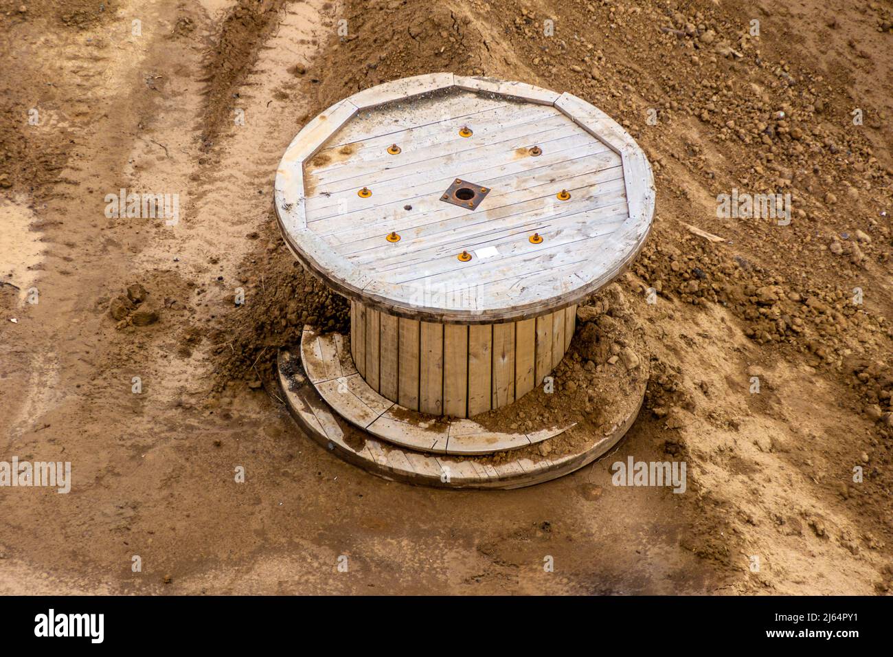 a large empty wooden reel from the cable lies on the clay soil of the construction site, selective focus Stock Photo