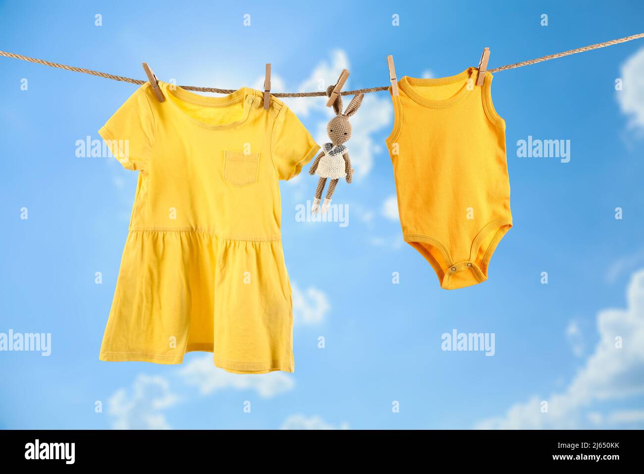 Baby clothes and toy hanging on rope against blue sky Stock Photo
