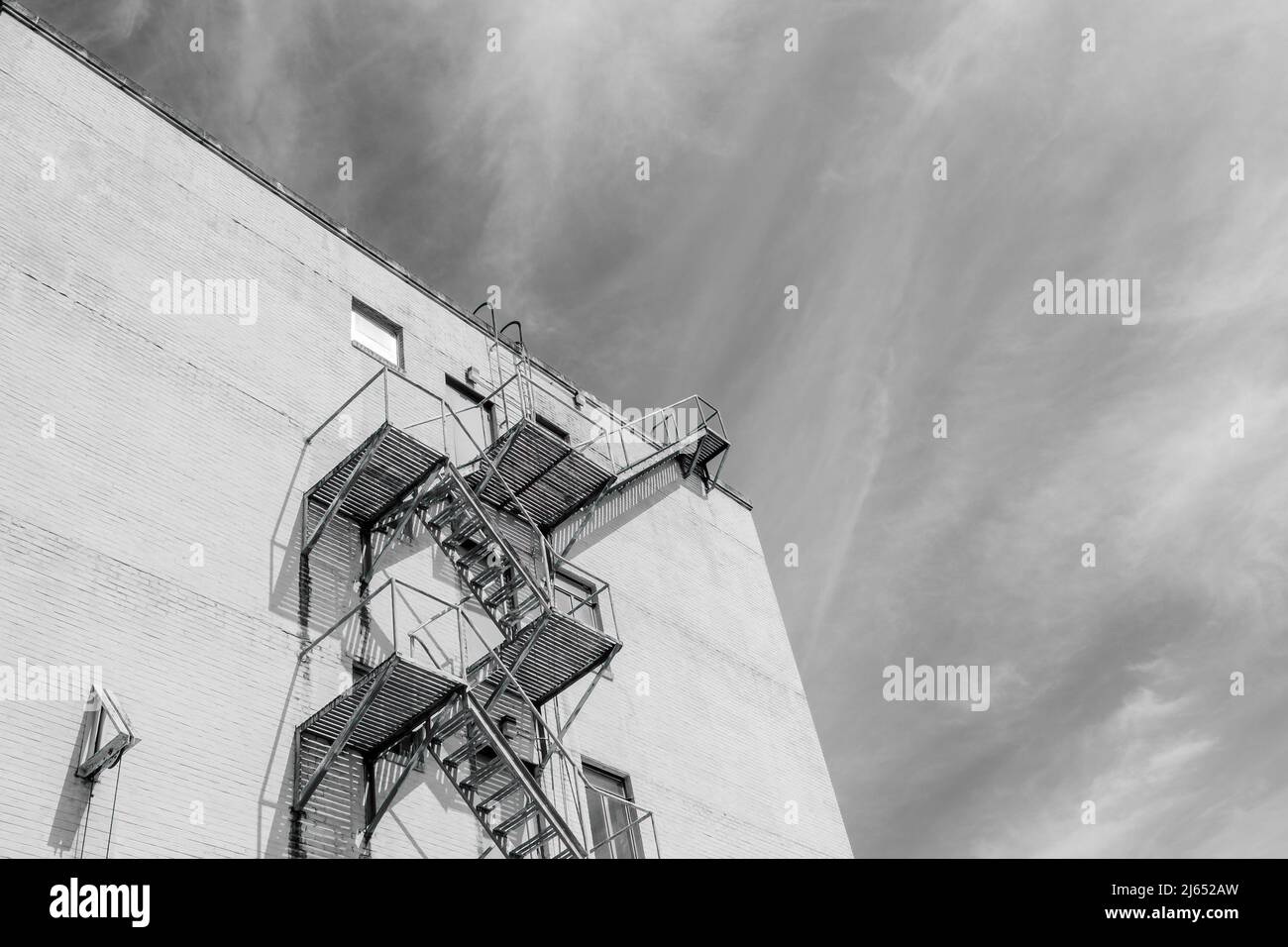 NEW ORLEANS, LA, USA - APRIL 19, 2022: Black and White image of a fire escape on the side of tall building and wispy clouds in the background Stock Photo