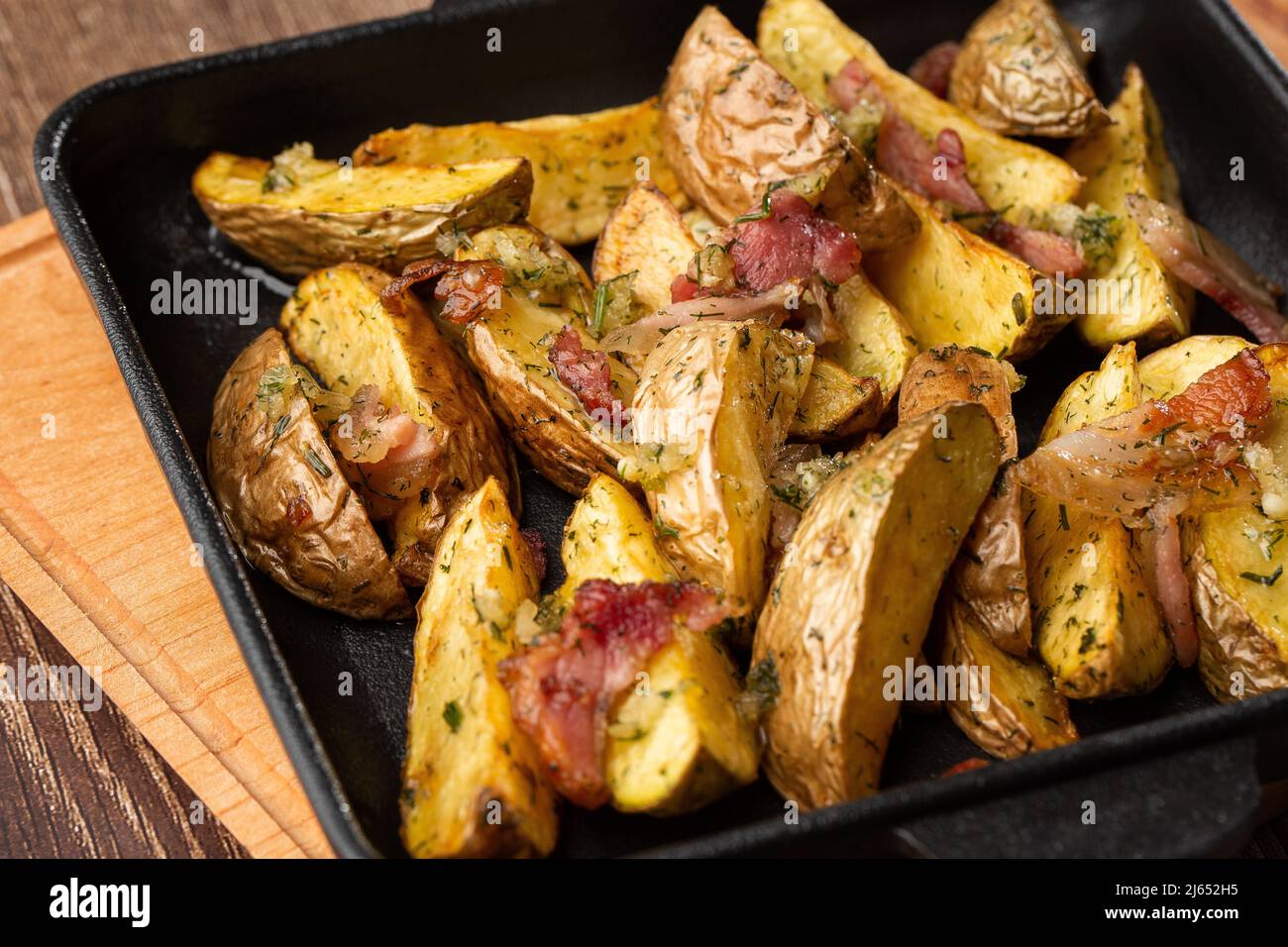 Delicious Fried Potato Bratkartoffeln With Bacon and Onion close up in the black plate on the table Stock Photo
